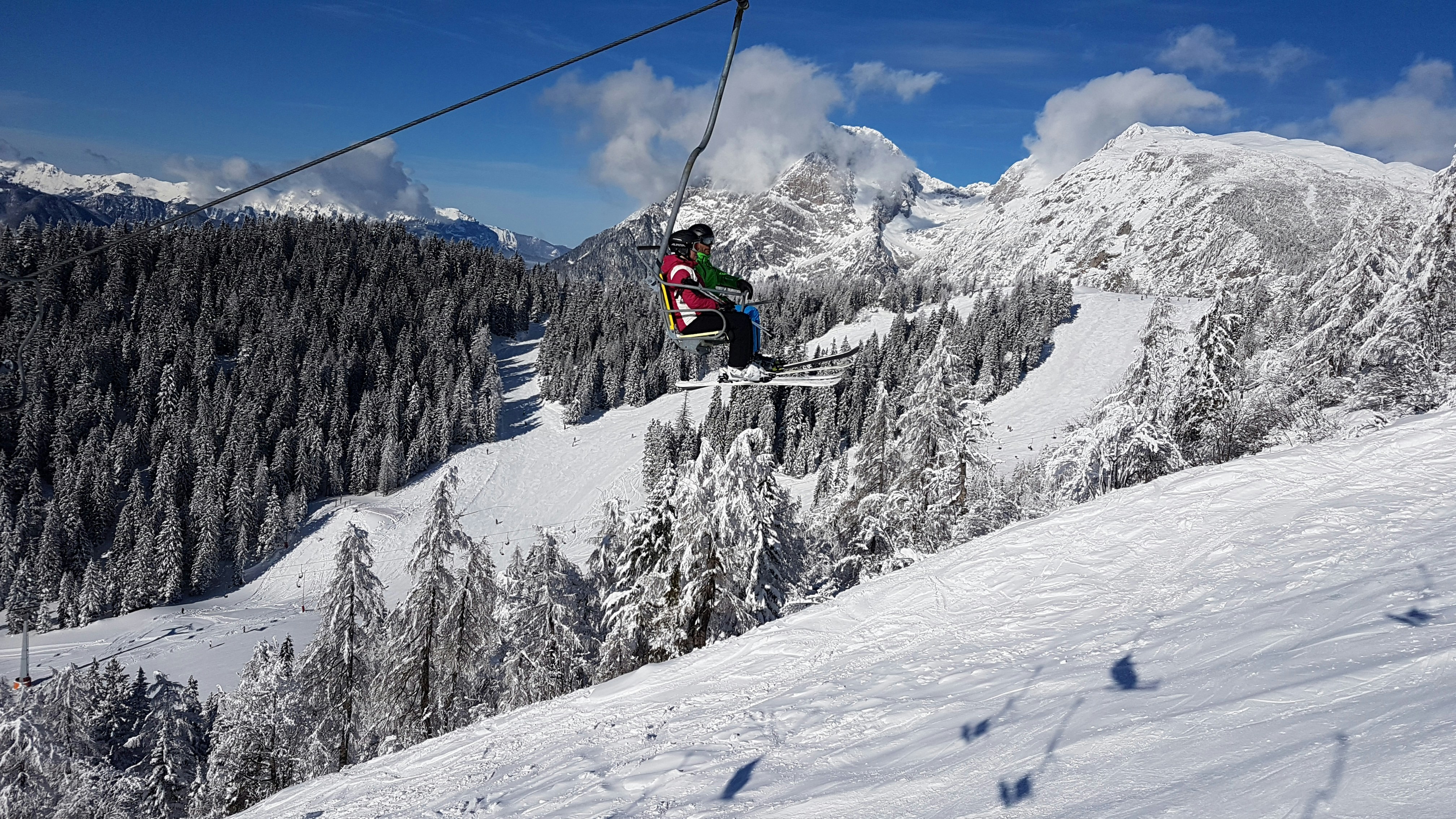 Skier riding a single chairlift high above a snow-covered slope and dense forest, highlighting the historic Mt. Eyak ski experience with Alaskan mountain views.